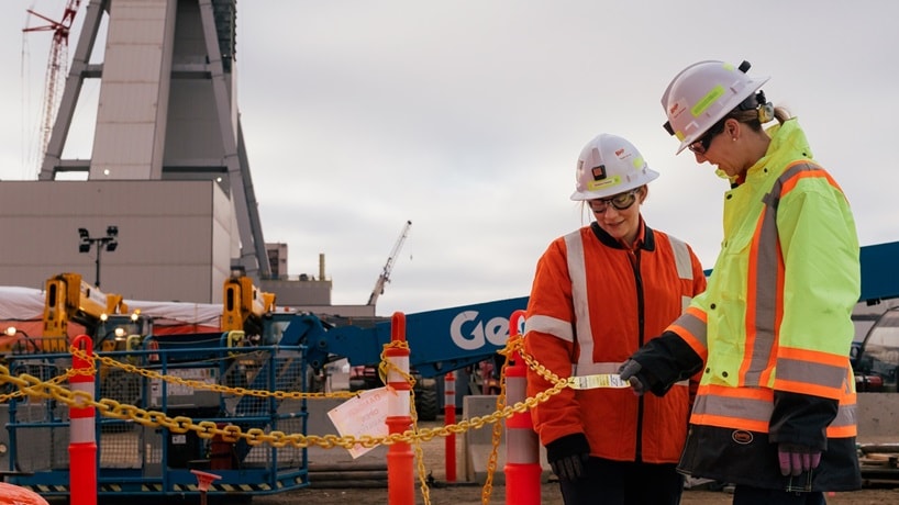Man and woman working at BHP Jansen with orange shirt and hats pointing at project plans